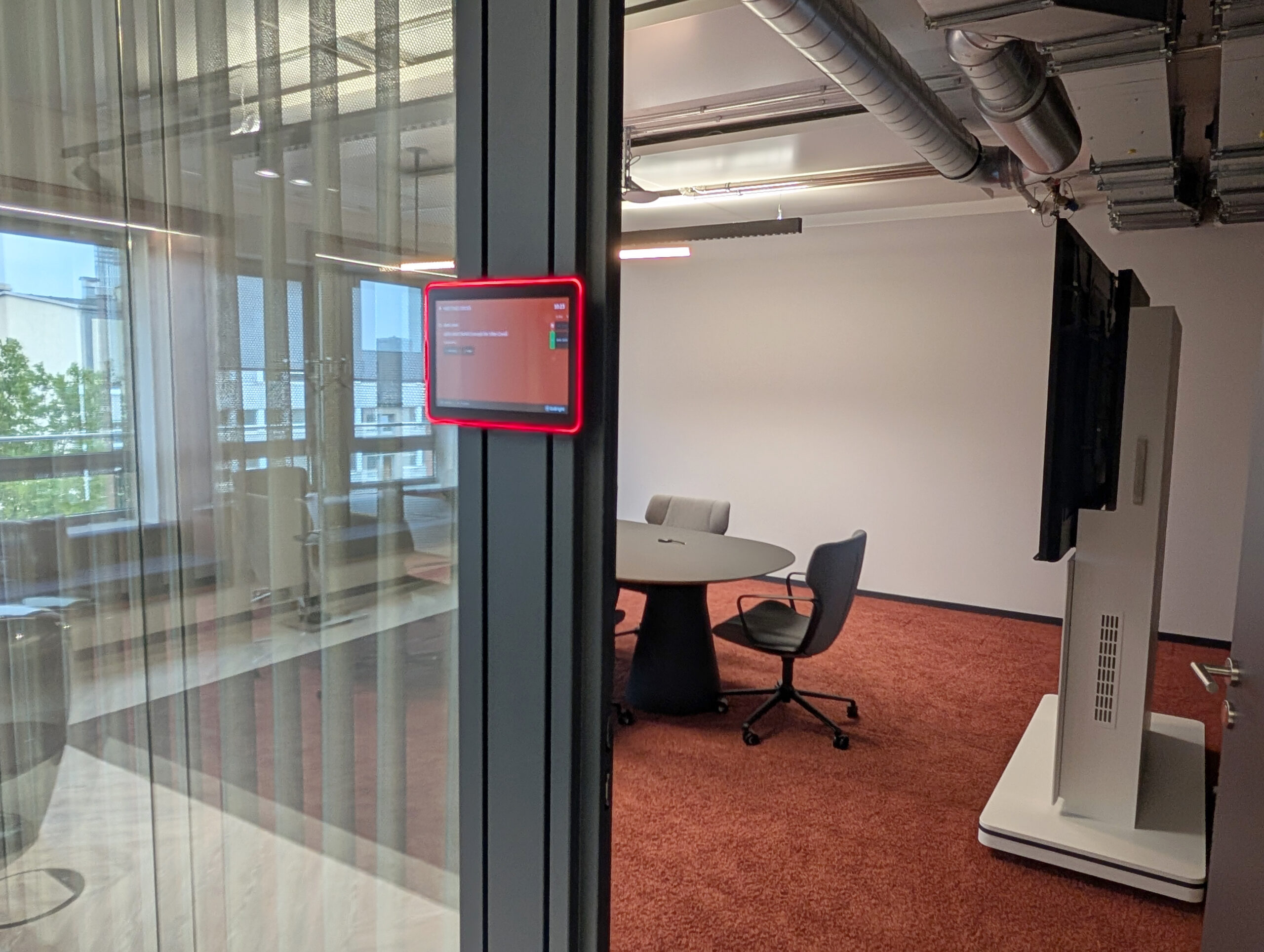 HEUSSEN Meetingraum 2 GoBright Raumbuchungsdisplay vor einem modernen Meetingraum